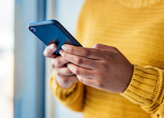 A person in a yellow sweater holding a cell phone in their hands